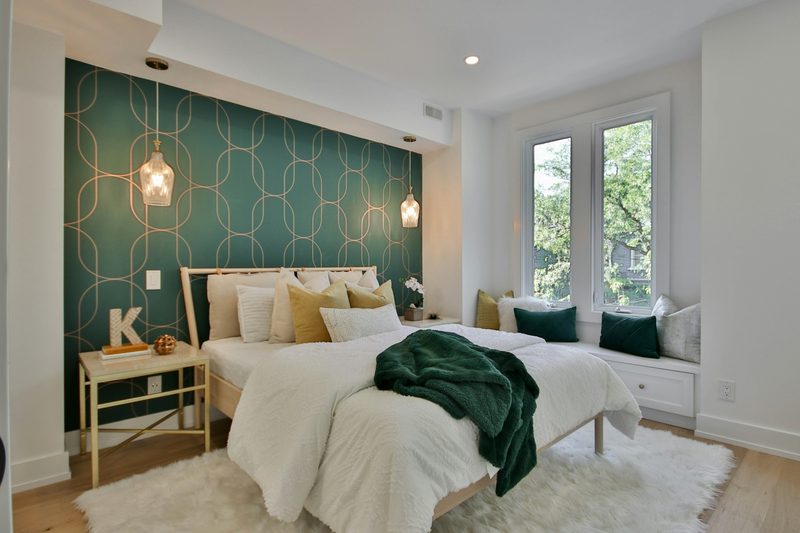Bright bedroom with a deep green and gold geometric wallpaper feature wall behind the bed, glass pendant lights and a window seat