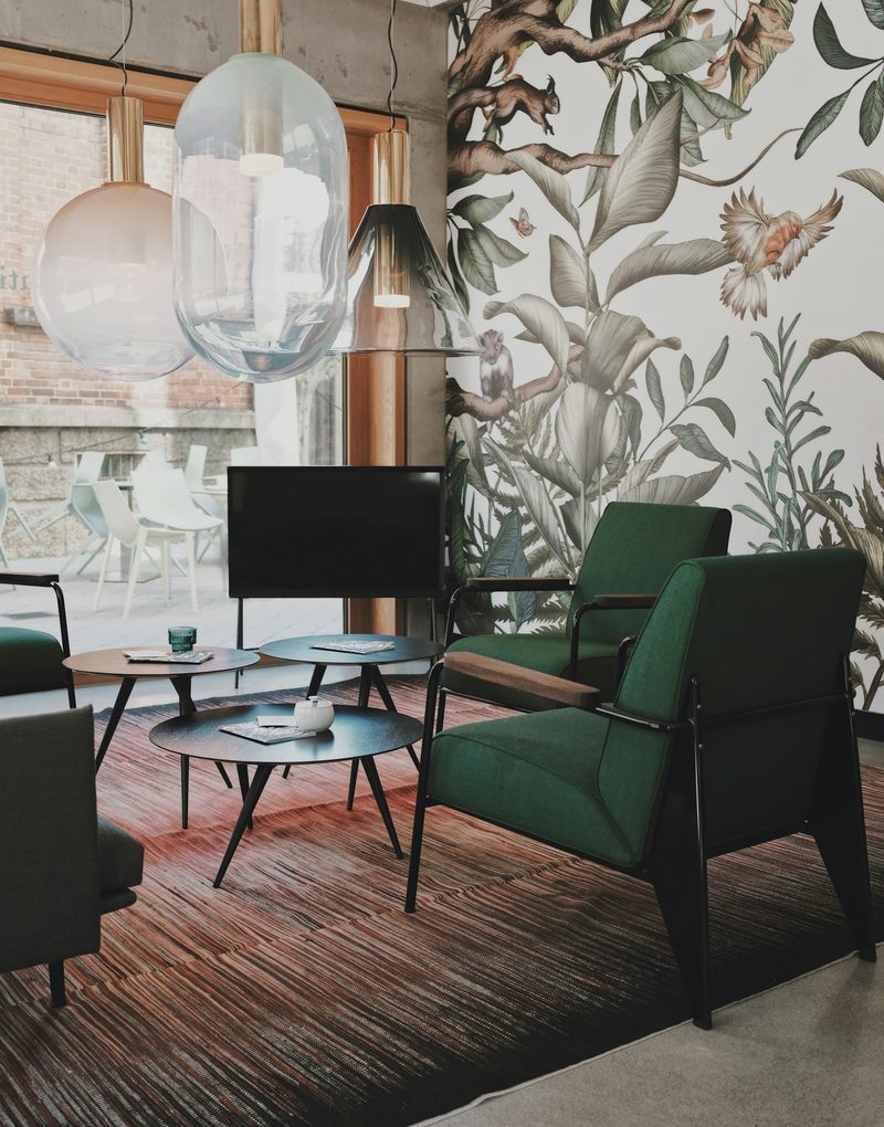 Lounge with a large-scale botanical mural wallpaper of leaves and birds, green armchairs and glass pendant lights