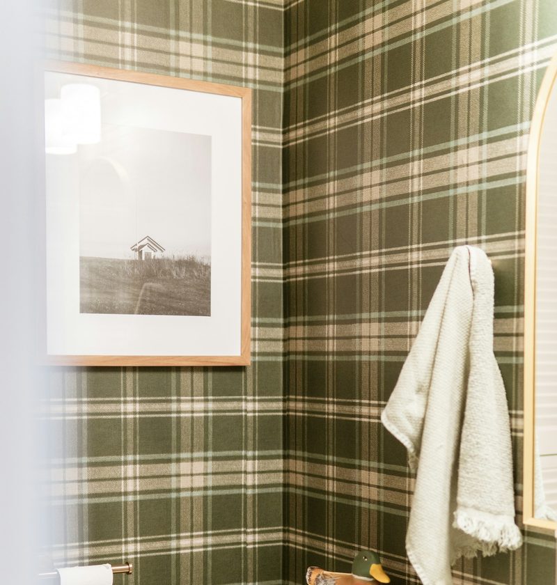 Powder room papered in a green and cream plaid wallpaper with a framed black-and-white photograph and a hanging towel