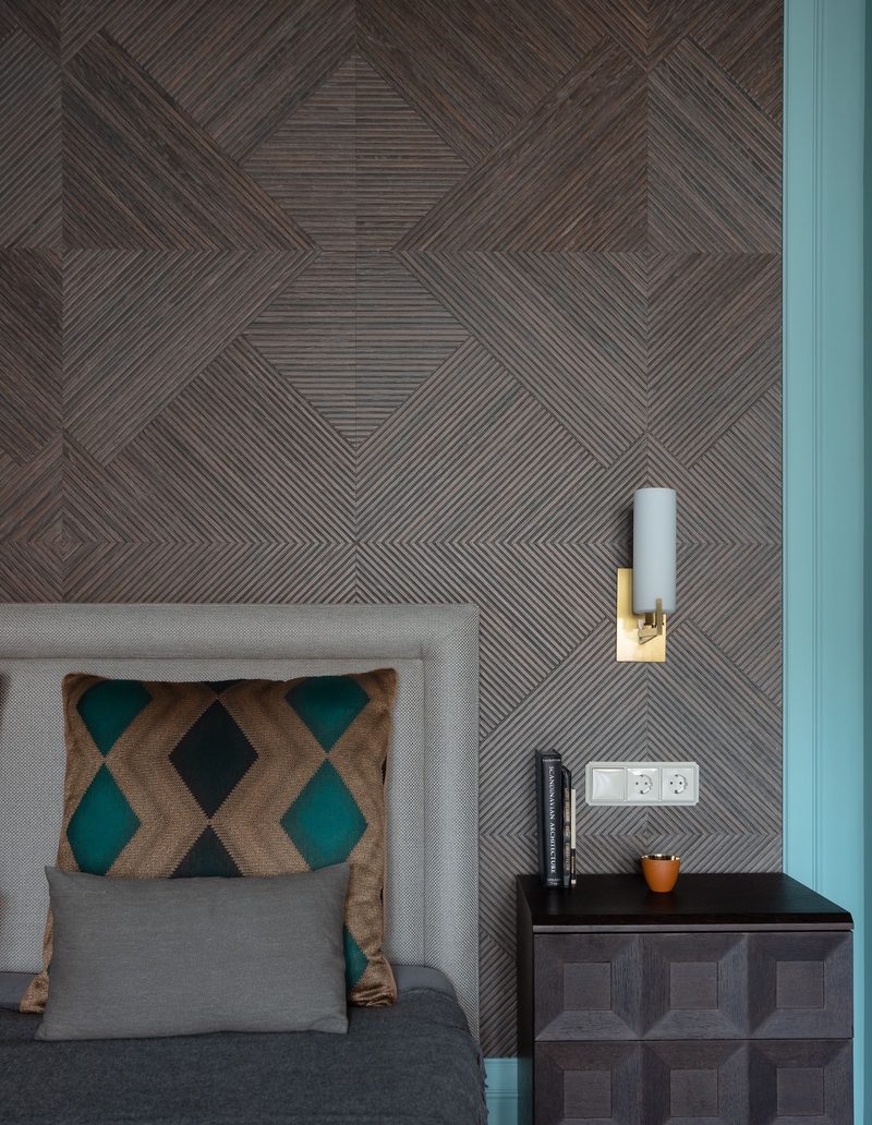 Modern bedroom corner with a textured wood-grain geometric wallpaper, a brass wall sconce and a dark geometric nightstand