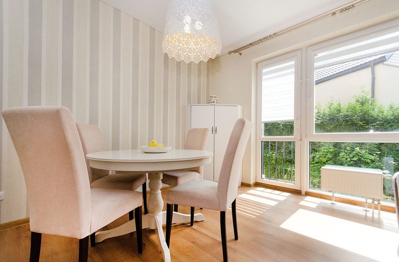 Bright dining area with a soft beige and white stripe wallpaper, a round pedestal table, blush upholstered chairs and floor-to-ceiling windows