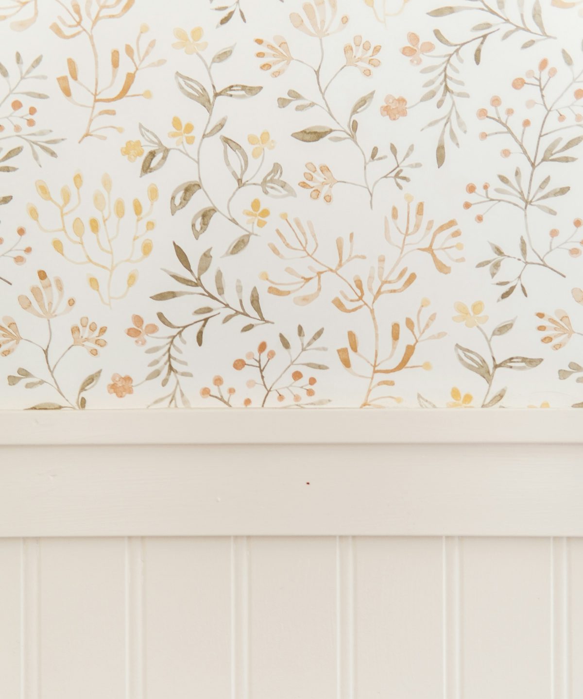 Close view of a small-scale botanical wallpaper in cream, sage and ochre meeting a painted cream beadboard wainscot and chair rail